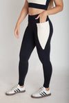 Legging fitness feminina preta e off white com bolsos laterais em Nagoya vista lateral com mão no bolso lateral
